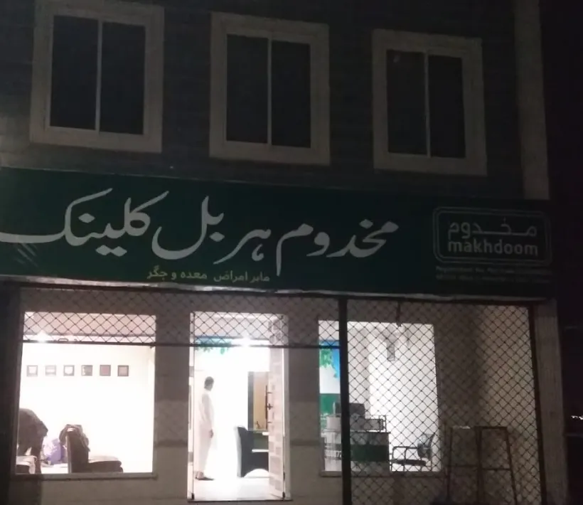 A green shop signboard with white Urdu lettering above a clinic, lit at night