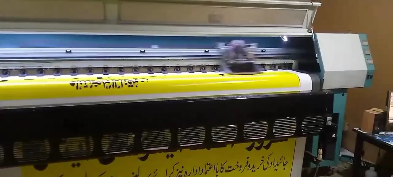 A large-format printer printing a yellow flex banner with Urdu lettering